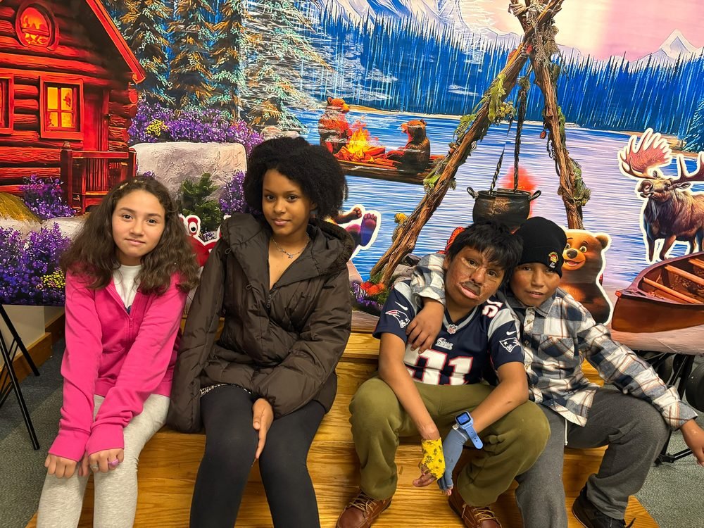 Four children sitting together in front of a colorful winter backdrop